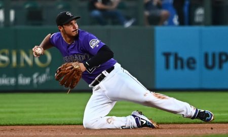 Nolan Arenado dives to his right, gets the ball, and is making a throwing motion to first or second base, wearing a purple Colorado Rockies jersey with white striped pants.