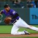 Nolan Arenado dives to his right, gets the ball, and is making a throwing motion to first or second base, wearing a purple Colorado Rockies jersey with white striped pants.