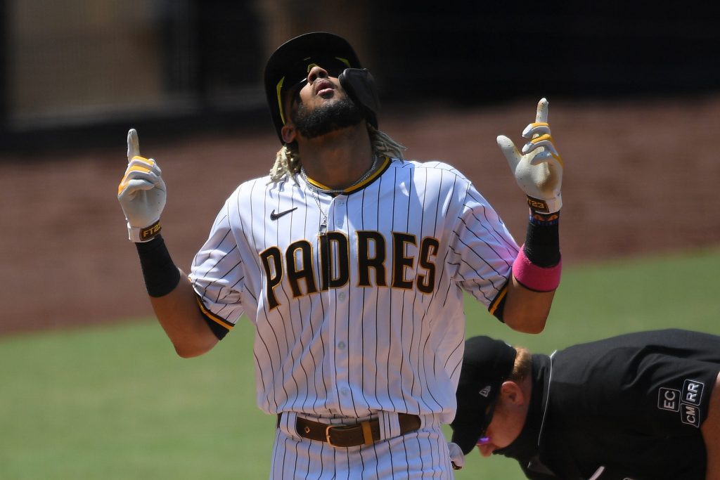 Fernando Tatis Jr. of the San Diego Padres pointing upward and celebrating a home run after crossing home plate. Umpire is in the background dusting off the plate.