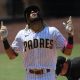 Fernando Tatis Jr. of the San Diego Padres pointing upward and celebrating a home run after crossing home plate. Umpire is in the background dusting off the plate.
